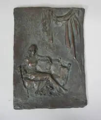 Bronze relief sculpture of a person seated in a chair with draped fabric hanging above to the right side.