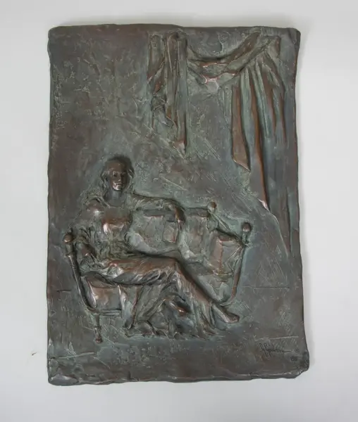 Bronze relief sculpture of a person seated in a chair with draped fabric hanging above to the right side.