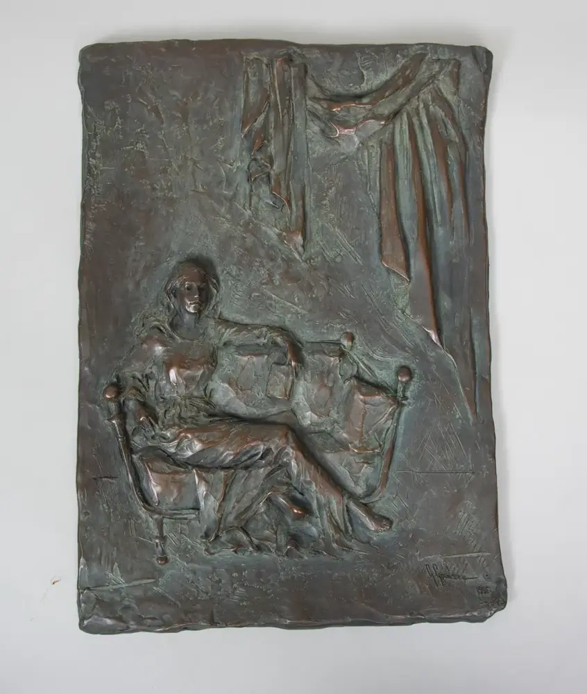 Bronze relief sculpture of a person seated in a chair with draped fabric hanging above to the right side.
