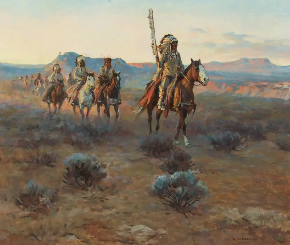 A line of Native American riders on horseback crosses a desert plain, led by a rider with a tall feathered headdress and staff, with distant mesas on the horizon.