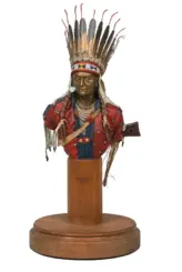 Bust of a Native American chief wearing a tall feather headdress and beadwork, displayed on a wooden pedestal