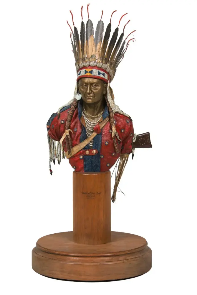 Bust of a Native American chief wearing a tall feather headdress and beadwork, displayed on a wooden pedestal