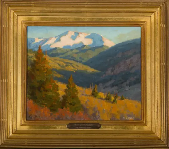 Framed landscape painting of a valley with colorful autumn trees, dark hills, and distant snow-capped mountains- golden frame visible around the scene.