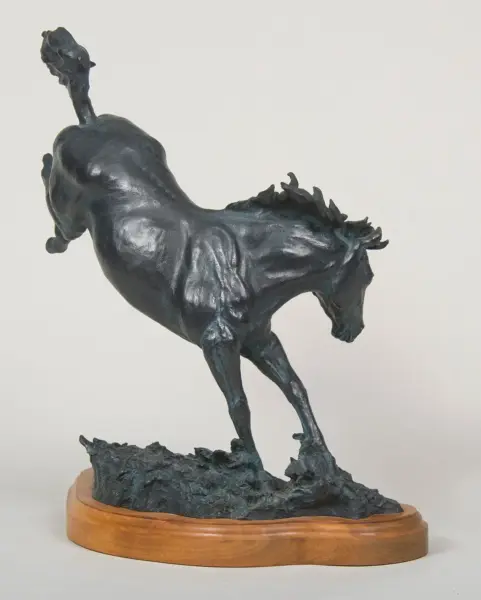 Bronze sculpture of a rearing horse on a textured rock base mounted on a wooden display pedestal