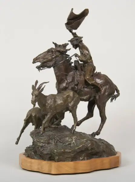 Bronze sculpture of a cowboy on a rearing horse, hat raised, with two other animals on a rocky base on a wooden plinth.