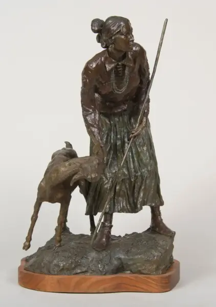 Bronze sculpture of a woman in a long skirt holding a staff, walking beside a dog on a rocky pedestal.