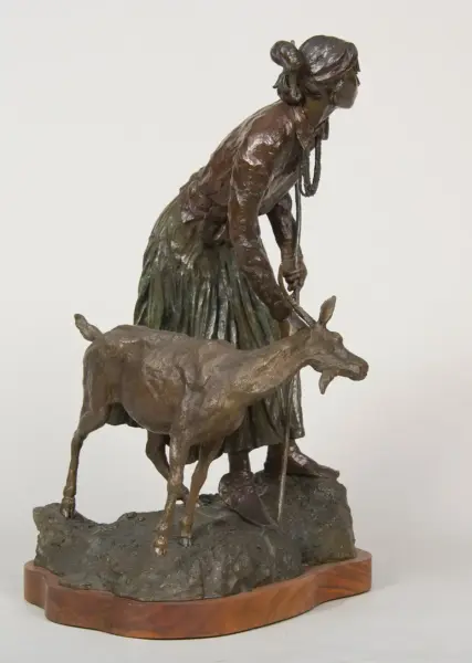 Bronze sculpture of a woman in a long dress bending to lead a deer on a rocky base, mounted on a wooden plaque