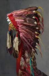 Person wearing a colorful feather headdress with red, pink, and yellow plumes against a gray backdrop.