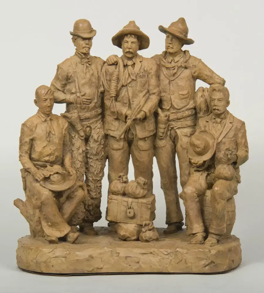 Clay sculpture of six men in old-time western outfits standing together on a base, with hats and rugged clothing.