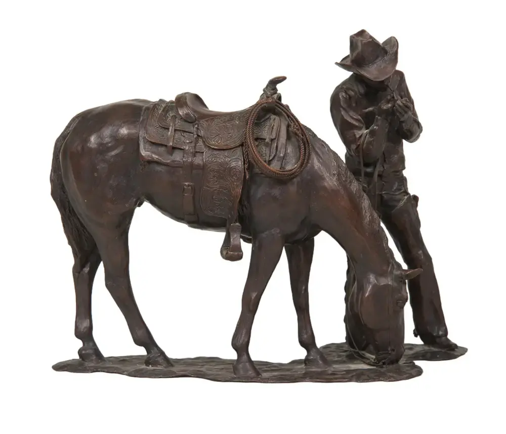 Bronze sculpture of a cowboy kneeling beside a saddled horse, with a rope hanging from the saddle.