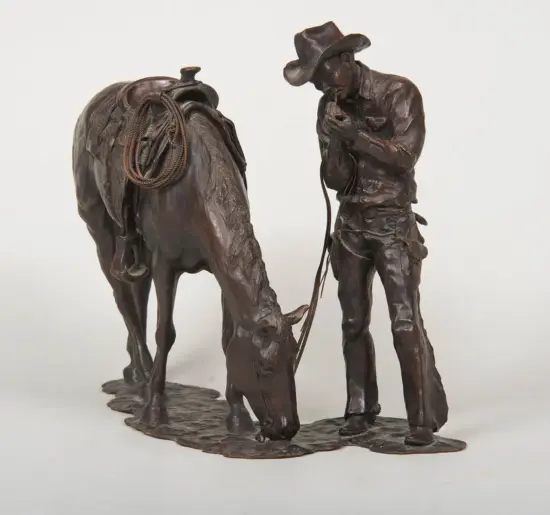 Bronze sculpture of a cowboy standing beside a saddled horse, holding the reins.