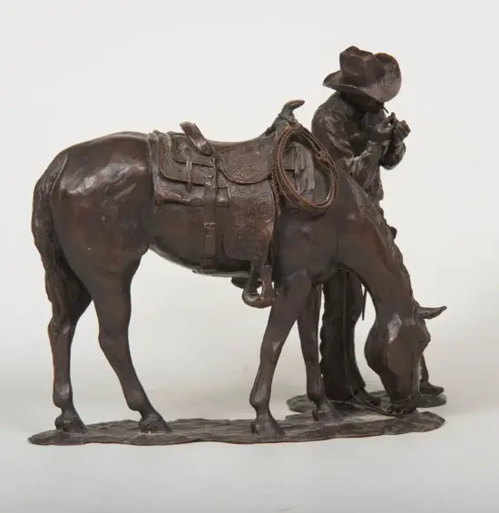 Bronze sculpture of a cowboy beside a saddled horse, horse head lowered, rope coiled at the saddle