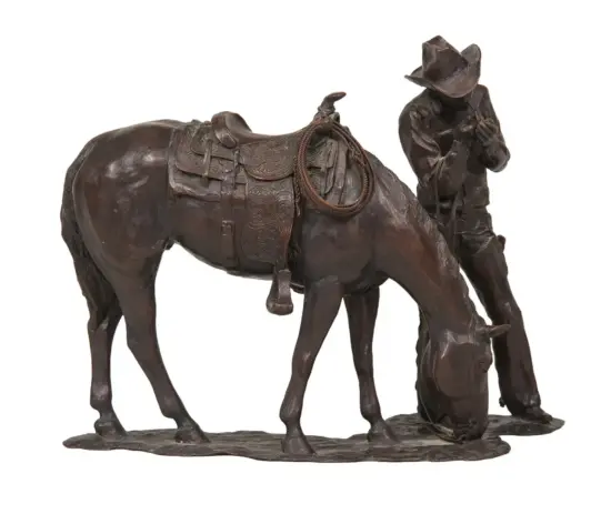 Bronze sculpture of a cowboy kneeling beside a saddled horse, with a rope hanging from the saddle.