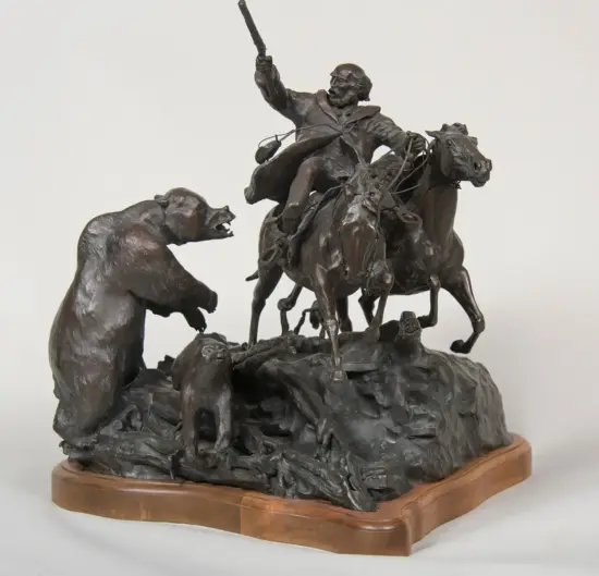 Bronze sculpture of a man on a galloping horse, sword raised, battling a bear on a rocky base.