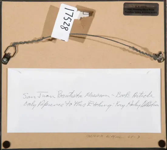 Back of a display frame with a twisted wire, a white tag with numbers, and a handwritten note on white paper beneath; a small address label sits in the upper-right corner.