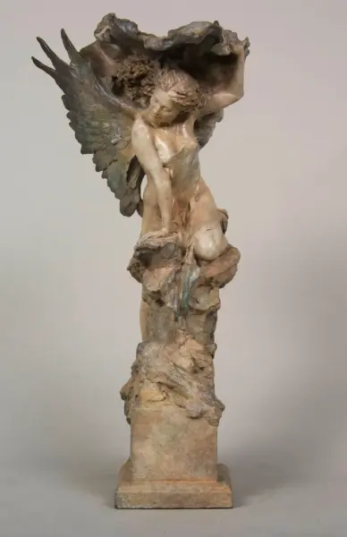 Sculpture of a kneeling angel with large wings, perched on a rocky pedestal.