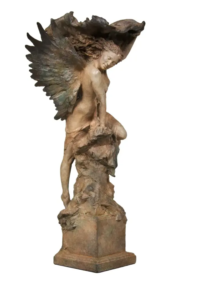 Bronze angel statue with large wings perched on a rocky pedestal, looking downward.