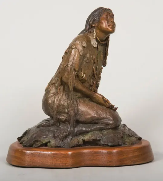 Bronze sculpture of a seated woman with flowing dress on a rocky base, mounted on a wooden pedestal
