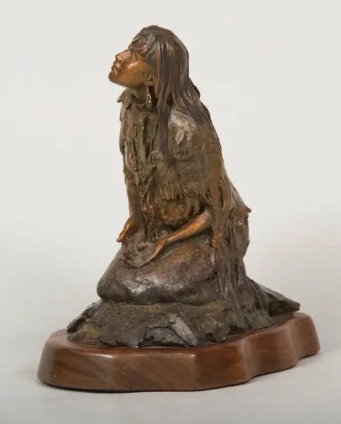 Bronze sculpture of a kneeling woman with long hair, head tilted upward, on a wooden base.