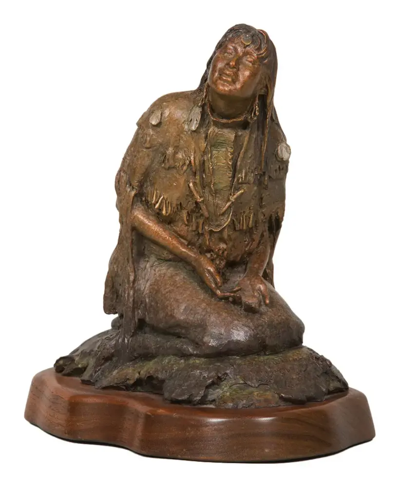 Bronze sculpture of a seated Indigenous woman with fringed clothing on a rocky base, mounted on a wooden pedestal