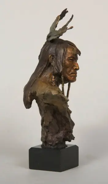 Bronze sculpture of a profile view man with a moose-like antler headdress on a black pedestal.