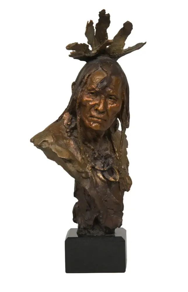 Bronze bust sculpture of a Native American figure with a feathered headdress on a black pedestal.