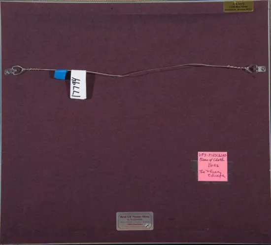 Back of a dark burgundy framed artwork with a routed metal hanging wire across the back, secured by blue tape and metal eyelets on each end; several small labels and a pink sticky note with handwritten text are visible.