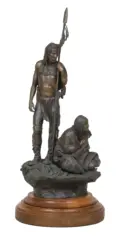 Bronze sculpture of a standing Indigenous man with a spear and a seated woman on a rocky base, mounted on a wooden pedestal.