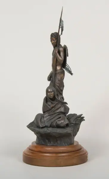 Bronze sculpture showing a standing man with a spear raised, behind a seated cloaked woman on a rocky base.