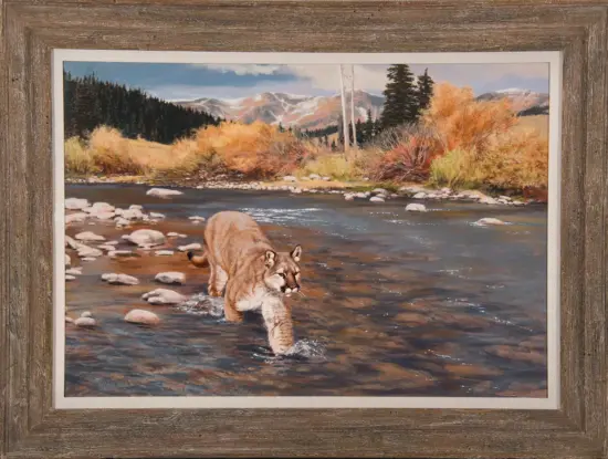 Painting of a mountain lion wading in a rocky river with autumn trees and distant snow-capped mountains in a rustic frame