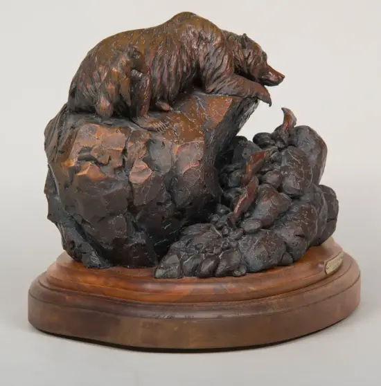 Bronze bear sculpture perched on a jagged rock formation mounted on a wooden pedestal.