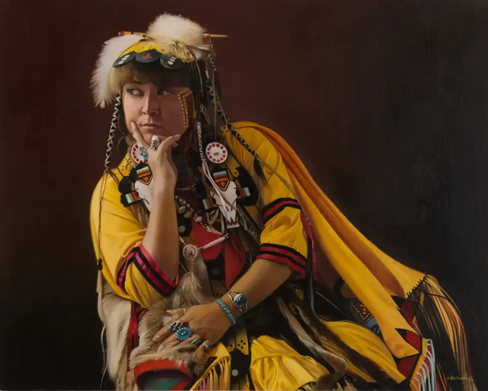 Portrait of a woman in colorful Native American ceremonial regalia with beadwork and feathers, resting her chin on her hand against a dark background.