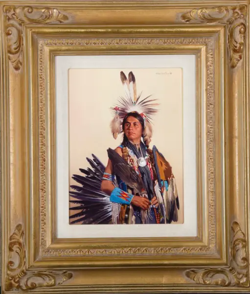 Portrait of a Native American man wearing a feather headdress and ceremonial regalia, framed in an ornate gold frame.