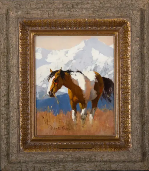 Pinto horse standing in a grassy field with snow-capped mountains in the background, framed by an ornate gold frame.