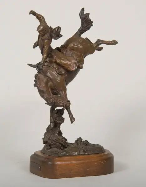 Bronze sculpture of a man riding a bucking horse, mounted on a wooden base.