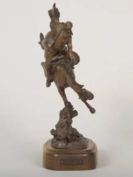 Bronze statue of a rider on a bucking horse, with the arm raised, mounted on a wooden pedestal.