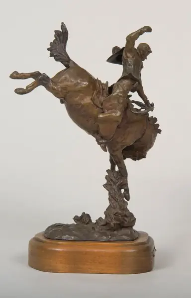 Bronze sculpture of a rider on a rearing horse, cape fluttering, mounted on a wooden base.