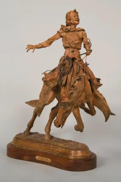 Bronze-toned sculpture of a cowboy riding a rearing horse, with a coiled rope at his waist, mounted on a wooden base