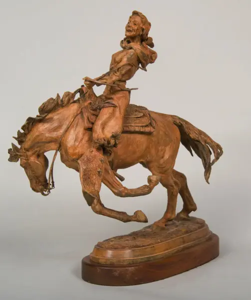 Wooden sculpture of a cowboy riding a rearing horse on a carved pedestal, with detailed saddle and reins.