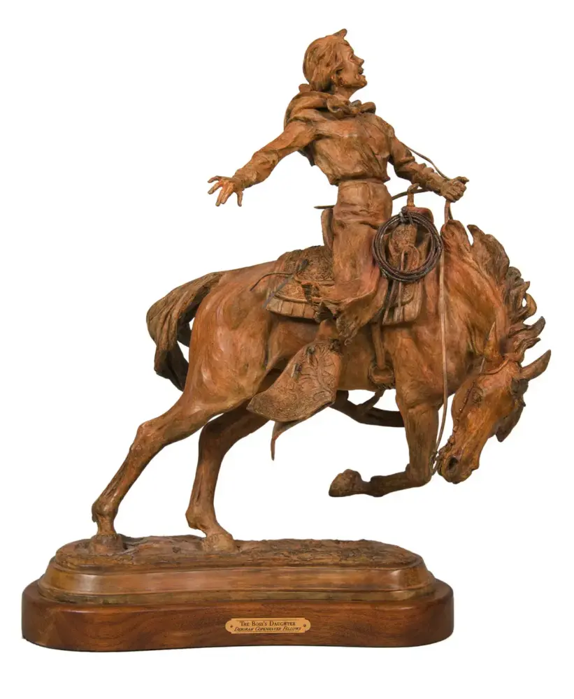 Bronze statue of a cowboy riding a bucking horse with a lasso, mounted on a wooden pedestal.