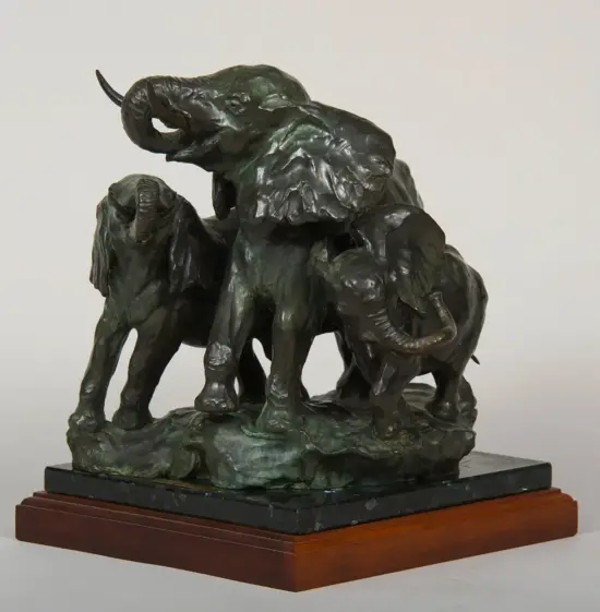 Bronze sculpture of a family of elephants, with an adult trunk raised and two calves, on a dark stone base with a wooden plinth.