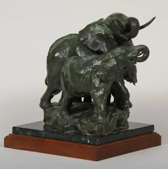 Bronze sculpture of two elephants with intertwined trunks, green patina, on a dark marble base with a wooden plinth.