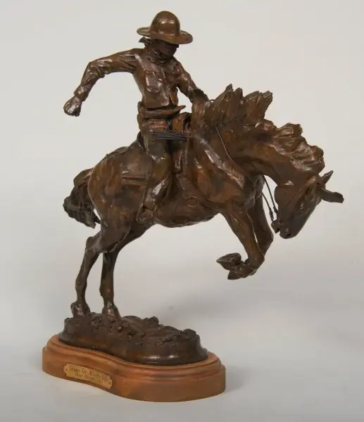 Bronze sculpture of a cowboy riding a bucking horse, mounted on a wooden base with a plaque that reads 'Start Of A Long Day'