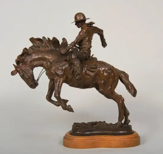 Bronze statue of a cowboy on a bucking horse, wearing a hat, gripping the reins mid-jump, mounted on a wooden base