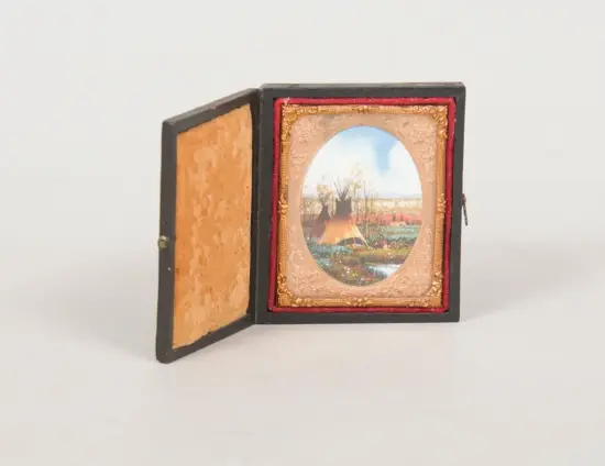 Small black hinged box opened to reveal a decorative circular landscape print in an ornate gold frame with red velvet lining on the inner edge.