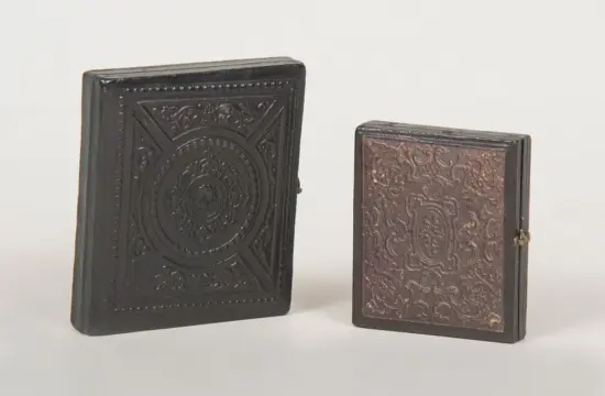 Two ornate, book-like boxes with embossed patterns, one large black on the left and a smaller brown one on the right.