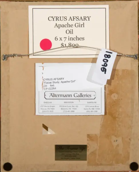 Back of a framed painting showing a label: 'CYRUS AFSARY Apache Girl Oil 6 x 7 inches $1,800' with a gallery card and a hanging wire across the back, plus a handwritten tag.