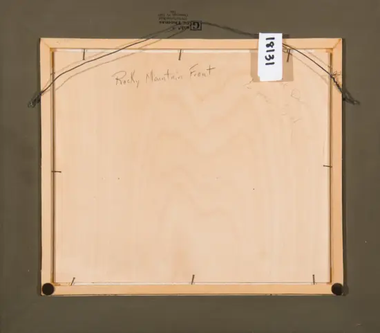 Back of a framed artwork showing the wooden frame, hanging wire across the top, and a white tag with numbers; handwritten note reads 'Rocky Mountain Front' on the back.