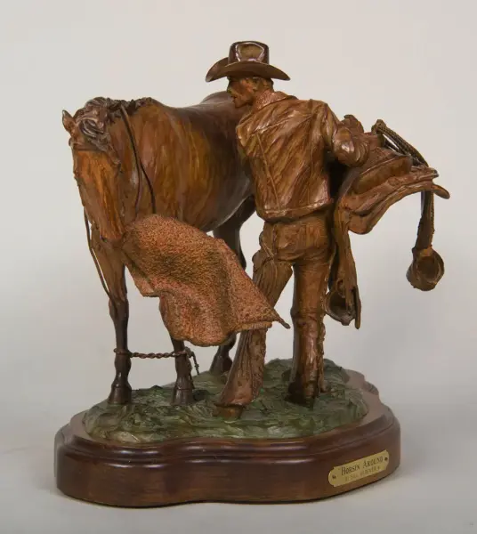 Bronze sculpture of a cowboy leaning toward a horse, with saddle and rope, on a textured green base with a plaque reading 'Horsin' Around' by Bill Nebeker.