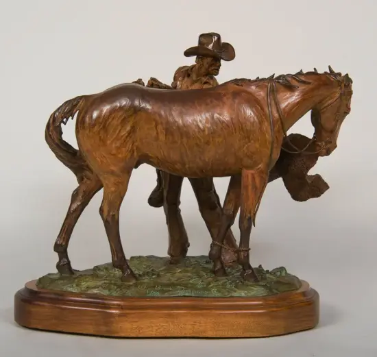 Bronze sculpture of a cowboy guiding a horse, mounted on a wooden oval base with a textured green pedestal surface.
